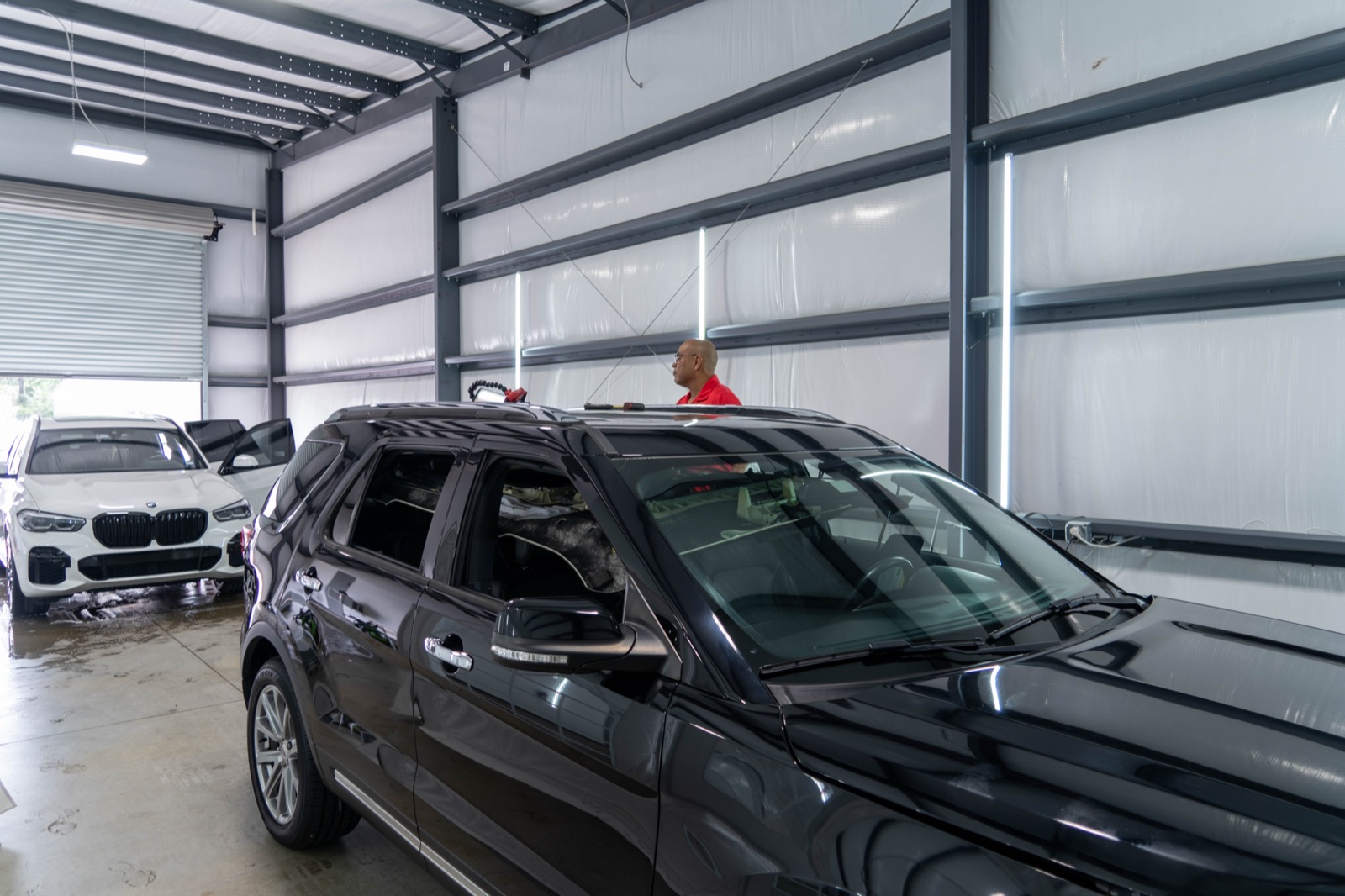 Auto Hail Techs shop bay with a black Ford Explorer and white BMW in for repair